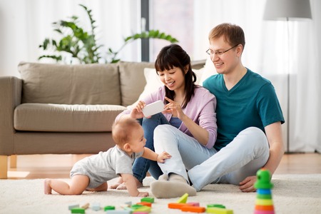 family, technology and people concept - happy mother and father taking picture or recording video of...