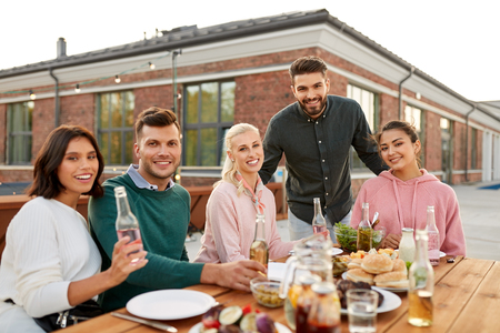 leisure and people concept - happy friends with drinks having barbecue or dinner party on rooftopの写真素材