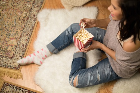 happy woman eating popcorn at homeの写真素材