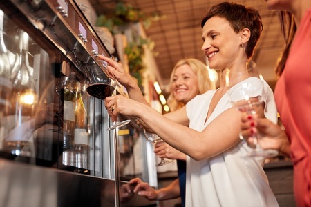 happy women pouring wine from dispenser at barの写真素材