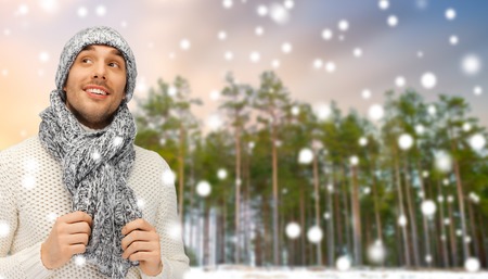 smiling man in hat and scarf over winter forestの写真素材