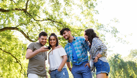 smiling friends with smartphone in summer parkの写真素材
