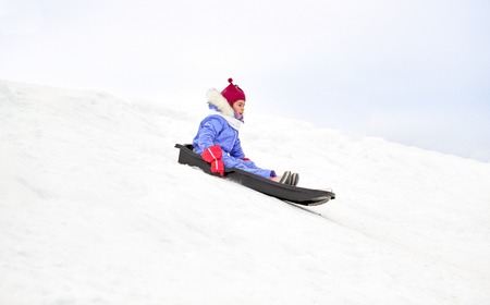 happy little girl sliding down on sled in winter