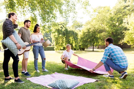 friends arranging place for picnic at summer parkの写真素材