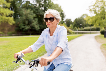 happy senior woman riding bicycle at summer parkの写真素材