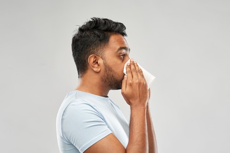 indian man with paper napkin blowing noseの写真素材