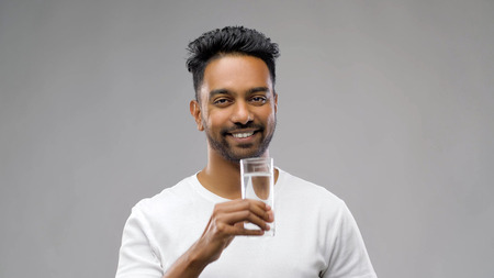 happy young indian man drinking water from glassの写真素材