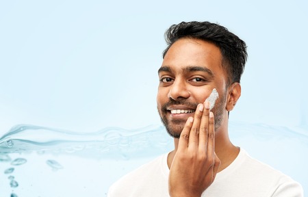 happy indian man applying cream to faceの写真素材