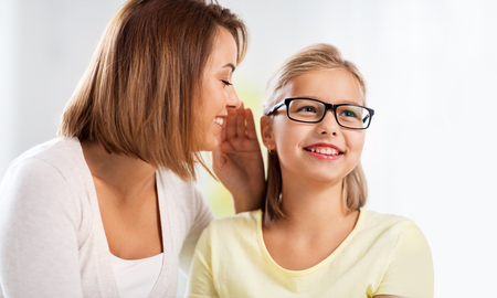 happy mother whispering secret to daughter at home