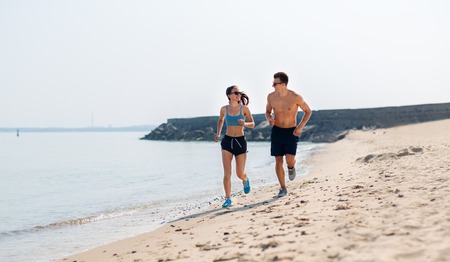 couple in sports clothes running along on beachの写真素材