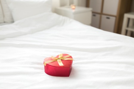 red gift box in shape of heart on bed at homeの写真素材