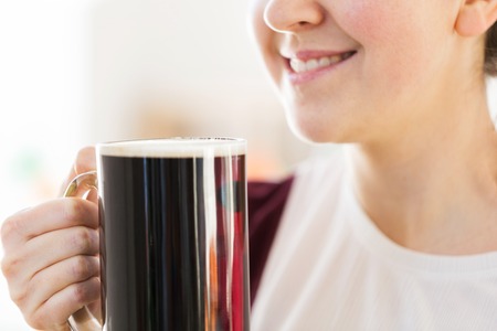 close up of smiling woman with dark beer in mug