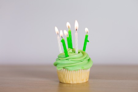 green cupcake with six burning candles on tableの写真素材
