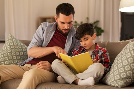 father and son reading book sofa at homeの写真素材