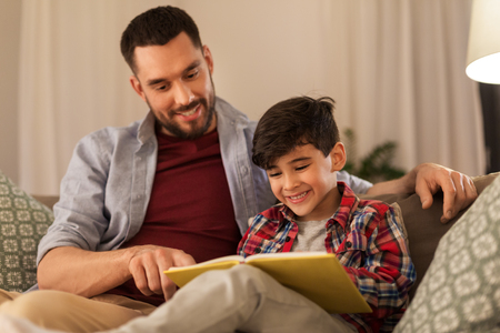 happy father and son reading book sofa at homeの写真素材
