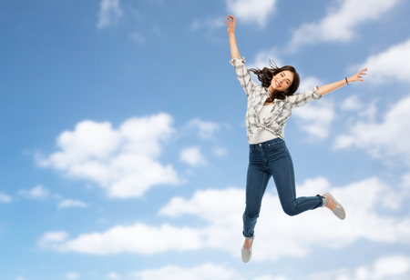 motion, freedom and people concept - happy young woman or teenage girl jumping over blue sky and clouds backgroundの写真素材