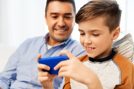 leisure, technology, family and people concept - happy father and son with smartphone playing game at homeの写真素材