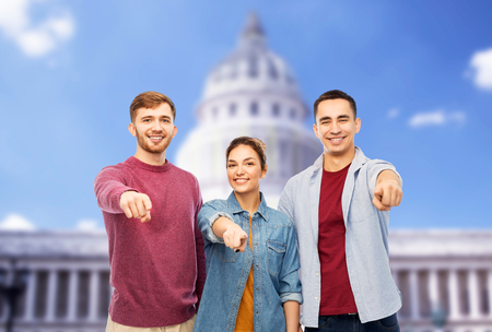 friendship and people concept - group of smiling friends pointing at you over capitol building...