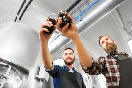 alcohol production, manufacture, business and people concept - male brewers clinking glasses of craft beer at breweryの写真素材