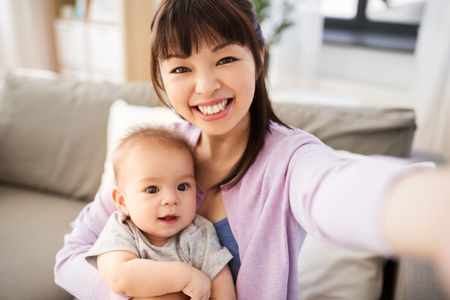 asian mother with baby son taking selfie at homeの写真素材