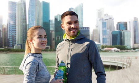 fitness, sport and people concept - smiling couple with bottles of water over singapore city marina backgroundの写真素材