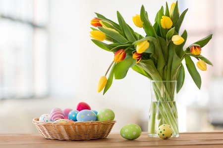 colored easter eggs in basket and flowers at homeの写真素材