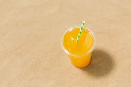 cup of orange juice with straw on beach sandの写真素材