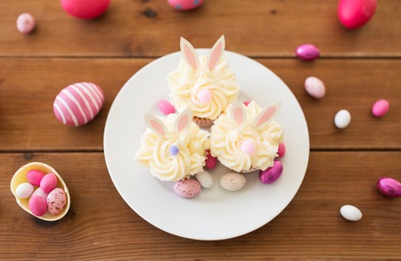 easter, food and holidays concept - frosted cupcakes with colored eggs and candies on wooden tableの写真素材