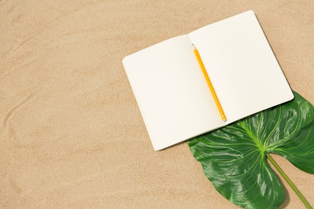 vacation, travel and summer concept - notebook with pencil and leaf on beach sandの写真素材