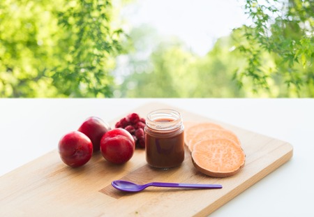 baby food, healthy eating and nutrition concept - fruit puree in glass jar with feeding spoon on wooden board over green natural backgroundの写真素材