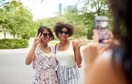 woman photographing her friends in summer parkの写真素材