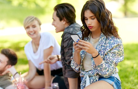 woman using smartphone at picnic with friendsの写真素材