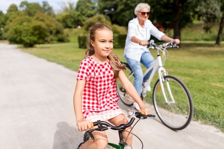 family, leisure and people concept - happy grandmother and granddaughter riding bicycles at summer parkの写真素材