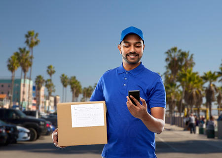 indian delivery man with smartphone and parcel boxの写真素材