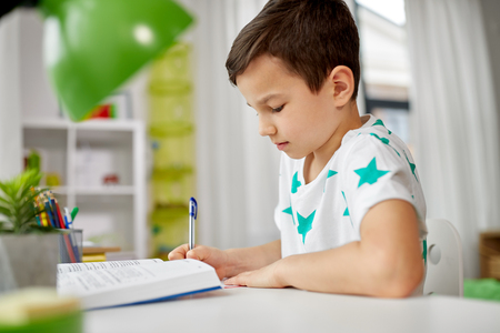 student boy with book writing to notebook at homeの写真素材