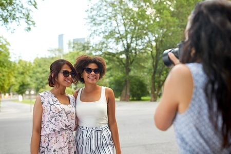 woman photographing her friends in summer parkの写真素材