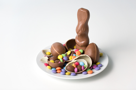 easter, sweets and confectionery concept - chocolate bunny, eggs and candy drops on white plateの写真素材