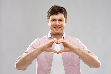 love, charity and valentine's day concept - smiling man making hand heart gesture over grey backgroundの写真素材