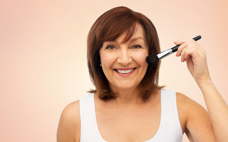 beauty, make up and old people concept - smiling senior woman with blush brush over beige backgroundの写真素材