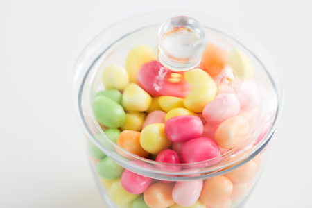 food, confectionery and sweets concept - close up of glass jar with colorful candy drops over white backgroundの写真素材