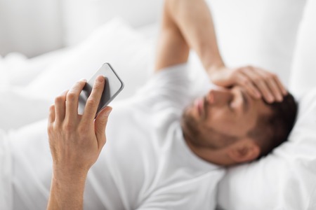hand of young man with smartphone in bedの写真素材