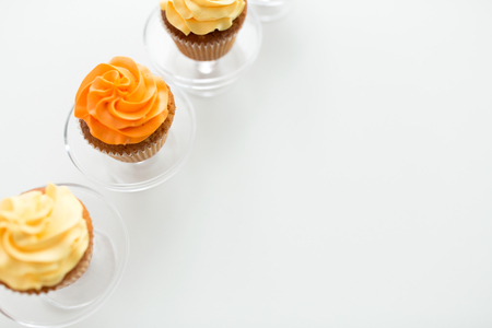 food, pastry and sweets concept - cupcakes with buttercream frosting on glass confectionery stand over white backgroundの写真素材