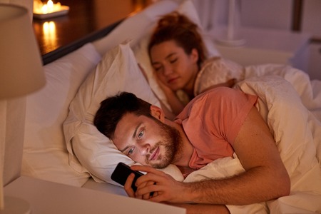 man using smartphone while girlfriend is sleepingの写真素材