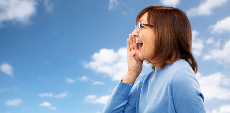 announcement and old people concept - senior woman in glasses calling over blue sky and clouds...