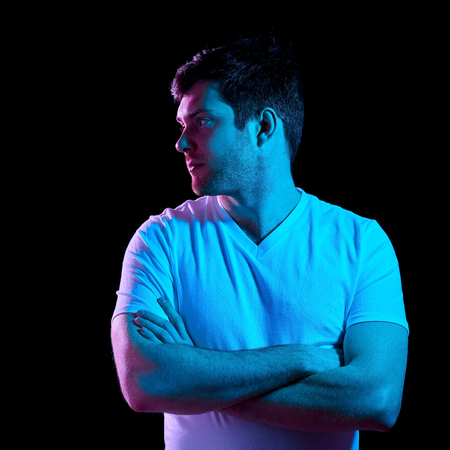 man with crossed arms over neon lights in darkness