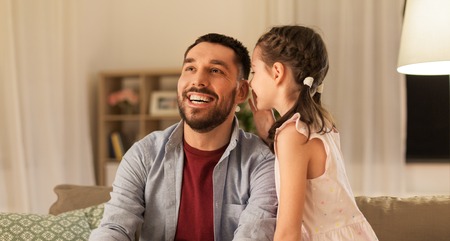 happy daughter whispering secret to father at home