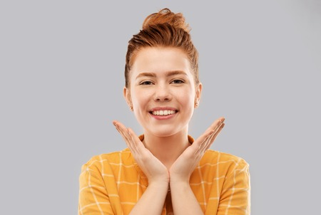 people concept - smiling red haired teenage girl in checkered shirt over grey background