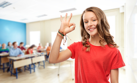 smiling teenage student girl showing ok at schoolの写真素材