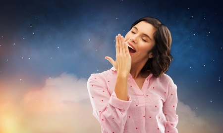 sleepy woman in pajama yawning over night skyの写真素材