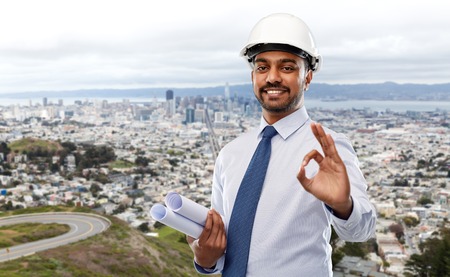 Architect in helmet with blueprints showing ok